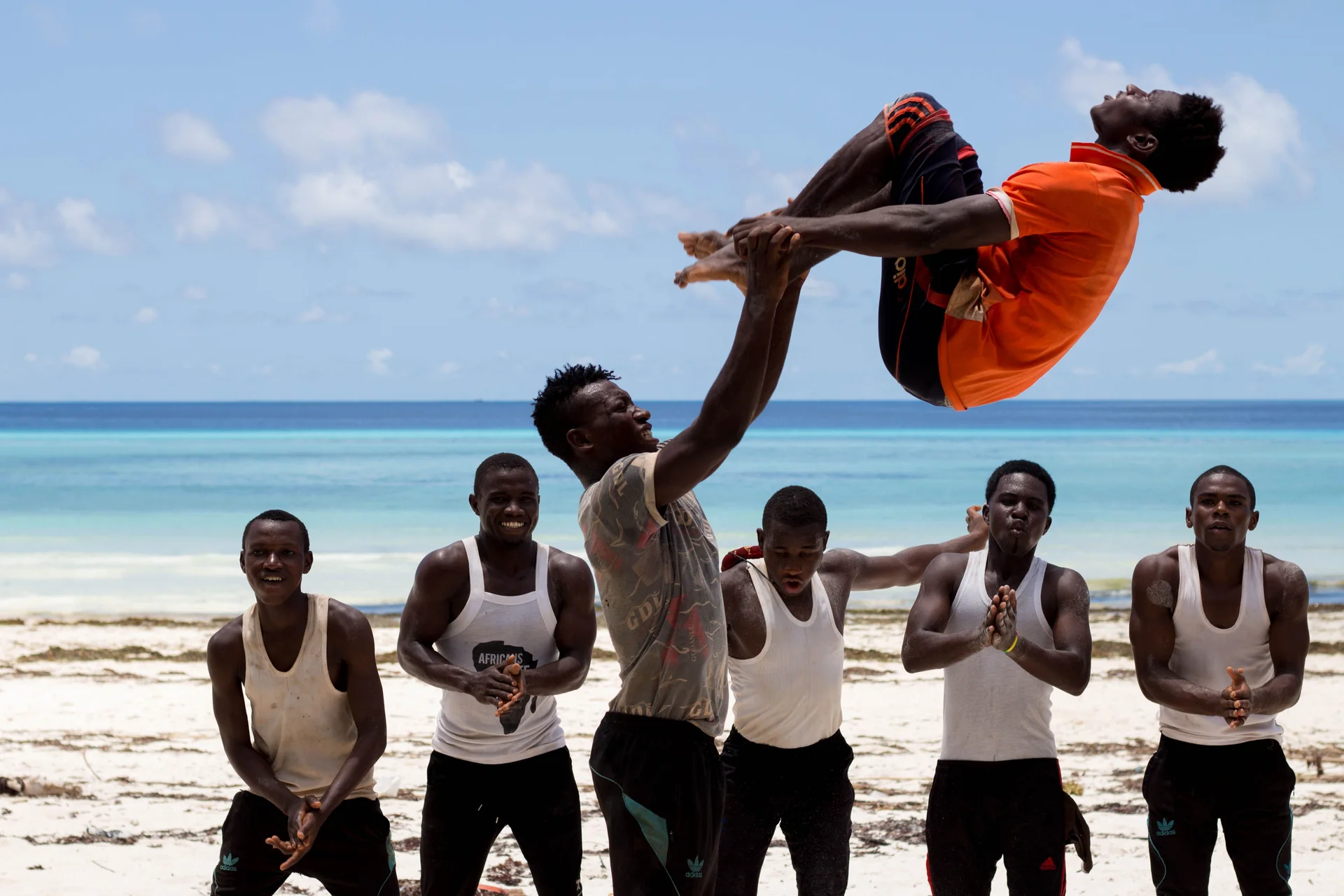 Trupa afrykańskich akrobatów wykonująca podnoszenie, jeden mężczyzna uniesiony wysoko nad kolegami z drużyny na plaży w Zanzibarze, Tanzania (zdjęcie poglądowe wschodnioafrykańskiej trupy akrobatów, nie sami wykonawcy Safari Cats)