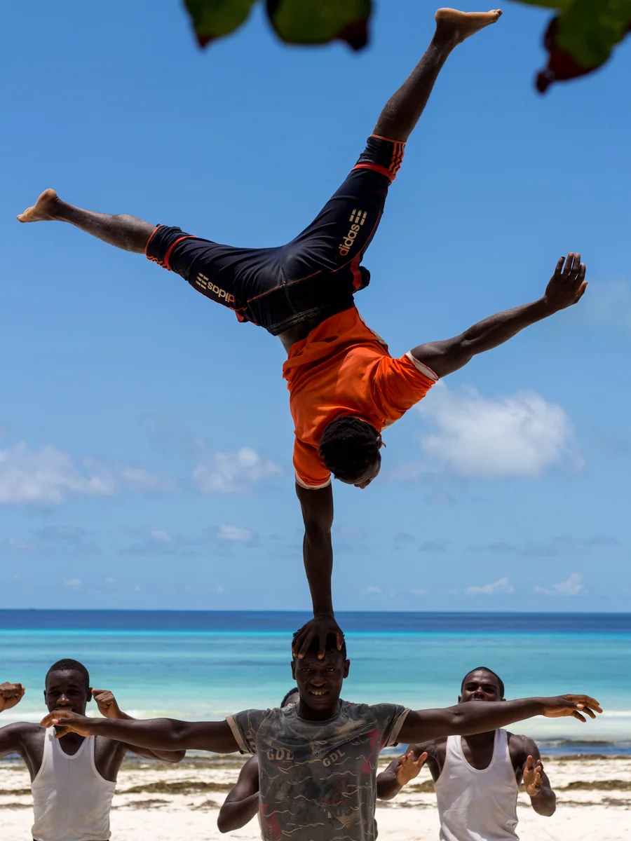 Akrobata wykonujący stanie na jednej ręce na głowie partnera, na plaży w Zanzibarze, Tanzania (reprezentatywne zdjęcie wschodnioafrykańskiej trupy akrobatycznej, nie Safari Cats)