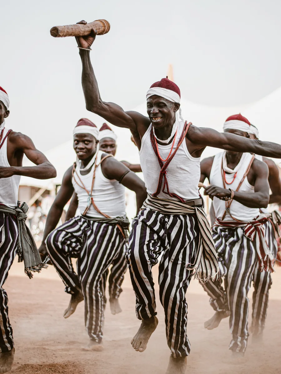 Tradycyjni tancerze w pasiastych strojach w połowie skoku podczas występu kulturalnego w Ilorin, Nigeria (reprezentatywne zdjęcie afrykańskiego tańca, nie własny układ Safari Cats)